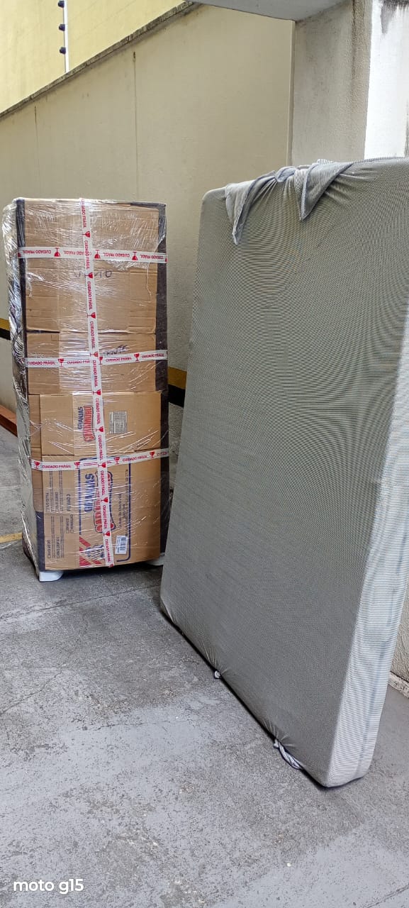 Pilha de caixas filmada e fitada ao lado de um colchão com capa de proteção